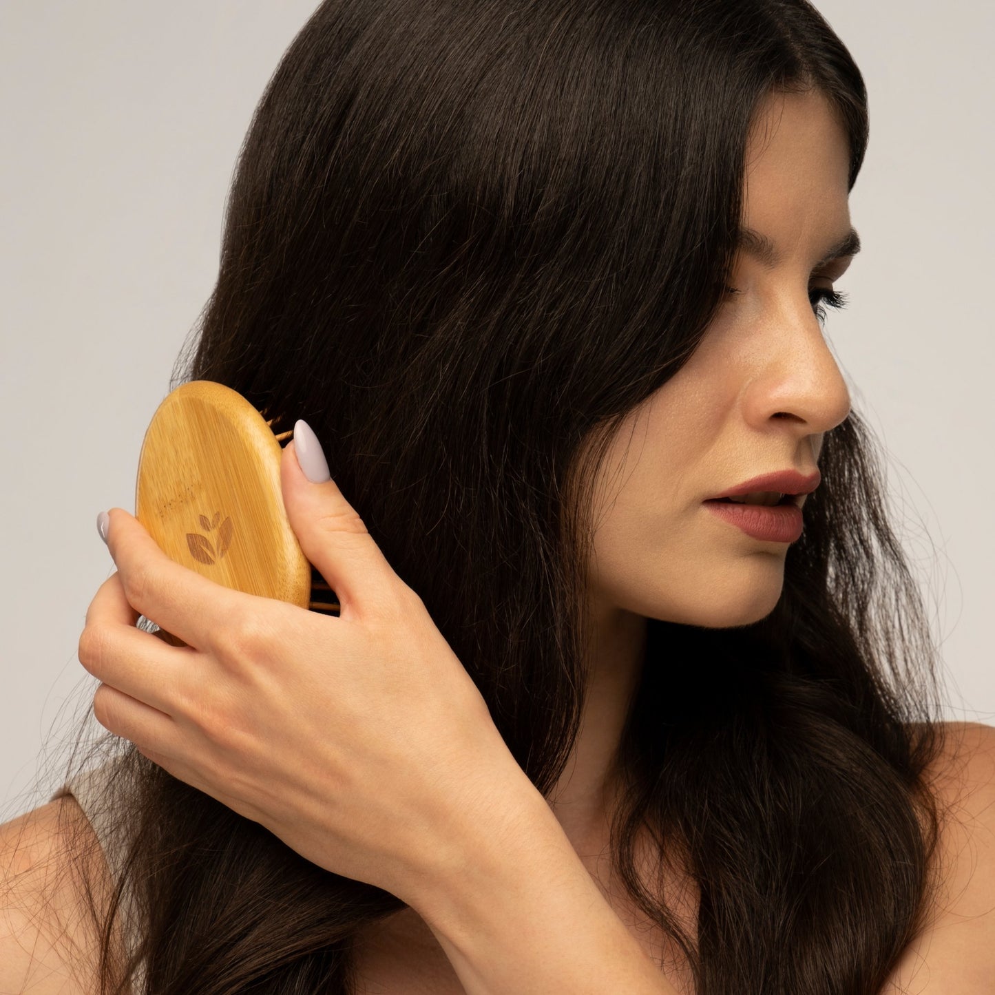 Eine Frau bürstet ihr langes, dunkles Haar mit einer Holzbürste und konzentriert sich auf die Haarpflege.