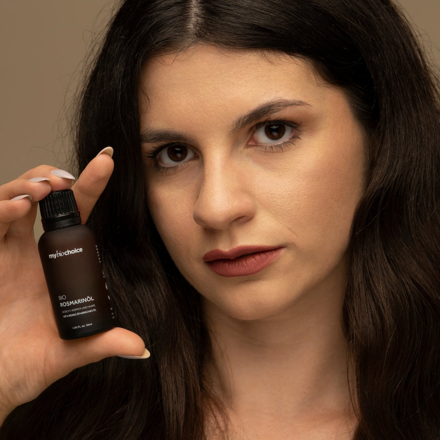 Eine Frau mit langem, dunklem Haar hält eine braune Flasche Bio Rosmarinöl von "mybiochoice" nahe ihrem Gesicht.