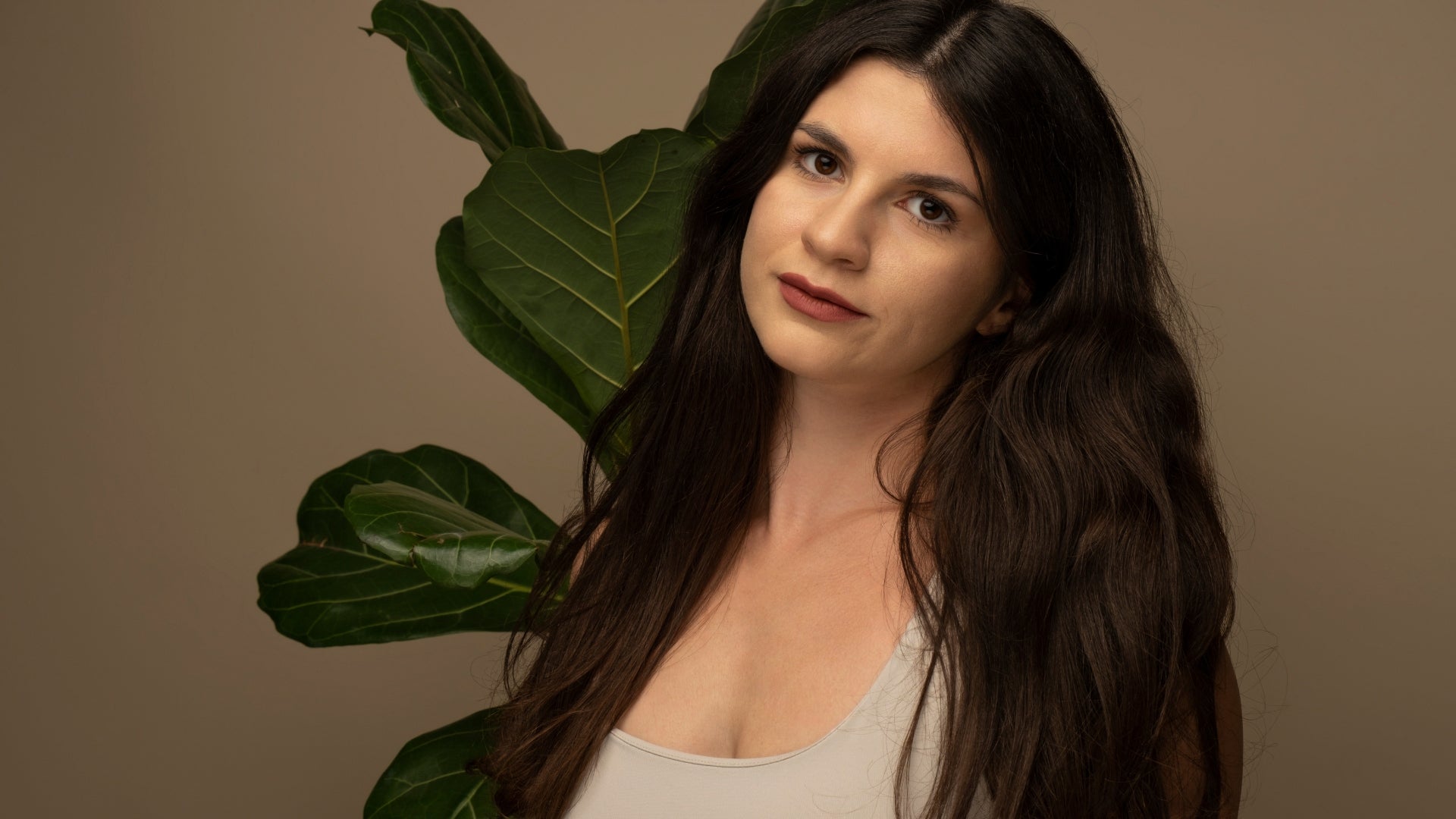 Porträt einer jungen Frau mit dunklem Haar vor einer grünen Pflanze – Gründerin einer Naturkosmetikmarke.