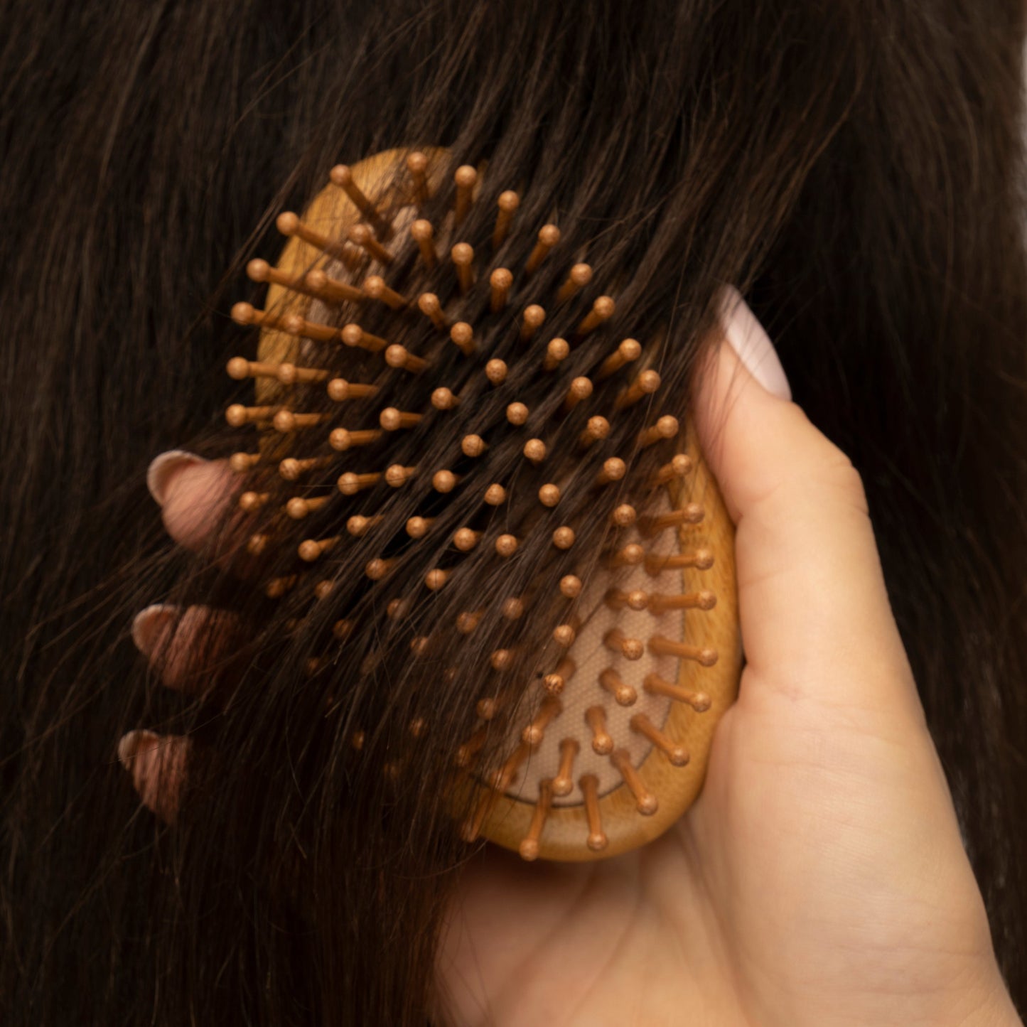 Nahaufnahme einer Hand, die dunkles Haar mit einer Holzbürste mit Bambusborsten bürstet.