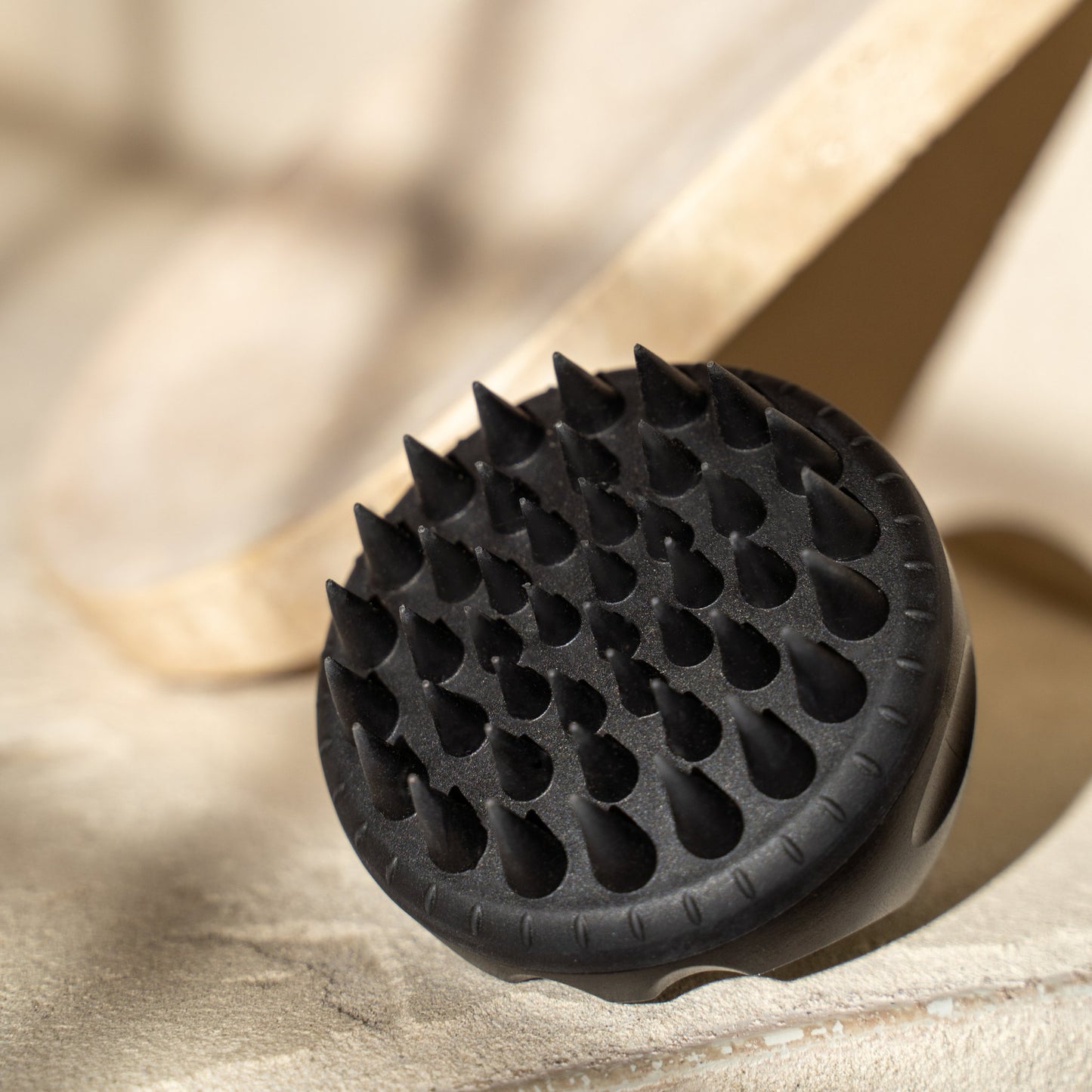 Nahaufnahme eines schwarzen Kopfhautmassagegeräts von mybiochoice mit spitzen Borsten auf einer hellen Steinoberfläche.